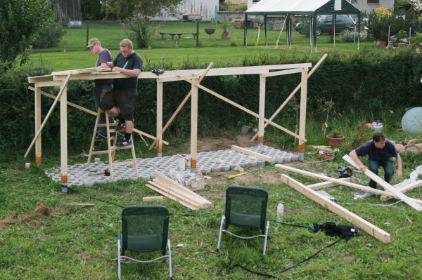 Blick auf das Grundgerüst des Holzlagers und zwei Leute beim Anbringen der Dachbretter